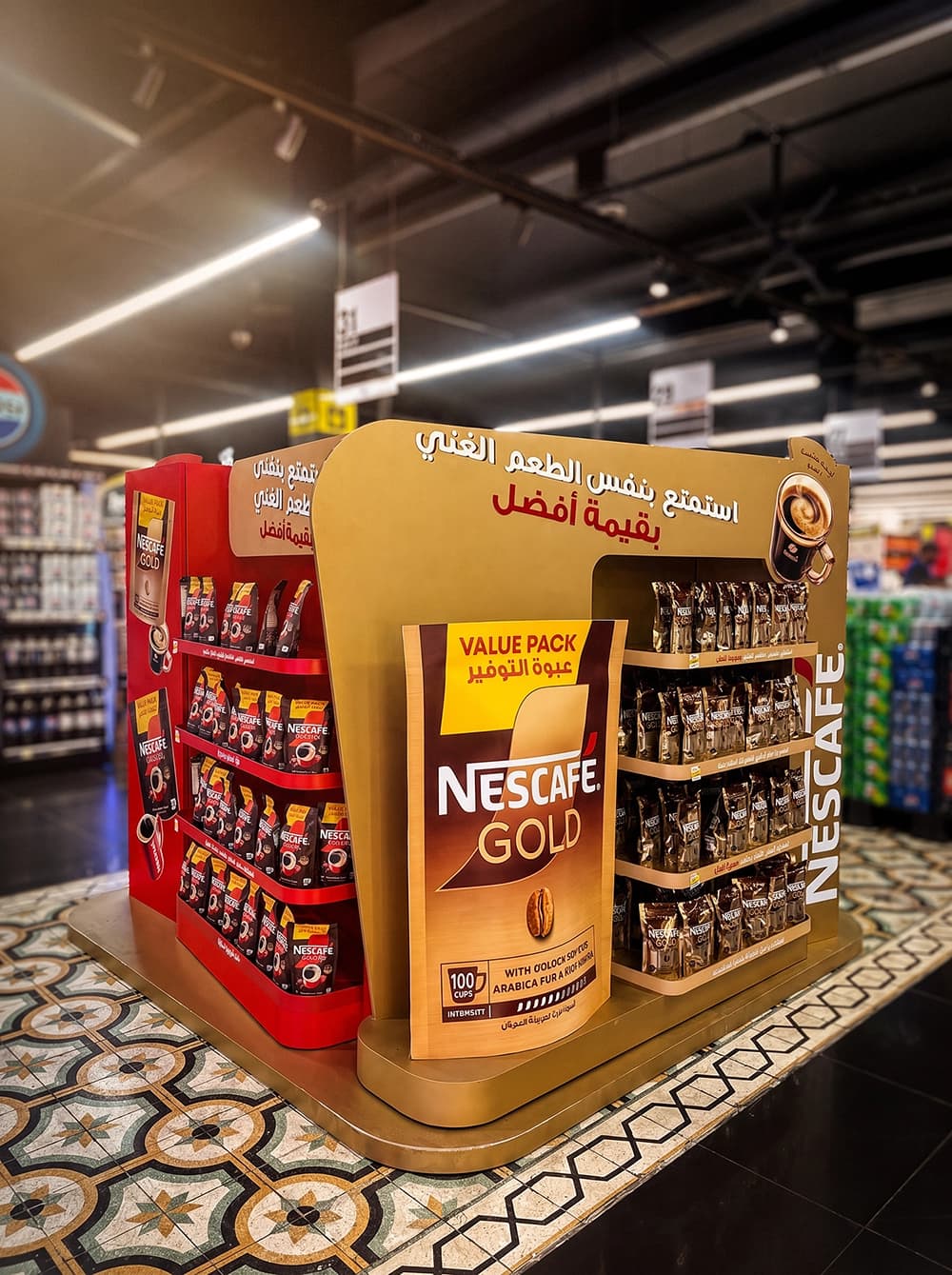 Nescafé freestanding display in a supermarket with gold shelving stocked with Nescafé Gold value packs, a red Nescafé Classic section and a curved gold header with Arabic messaging
