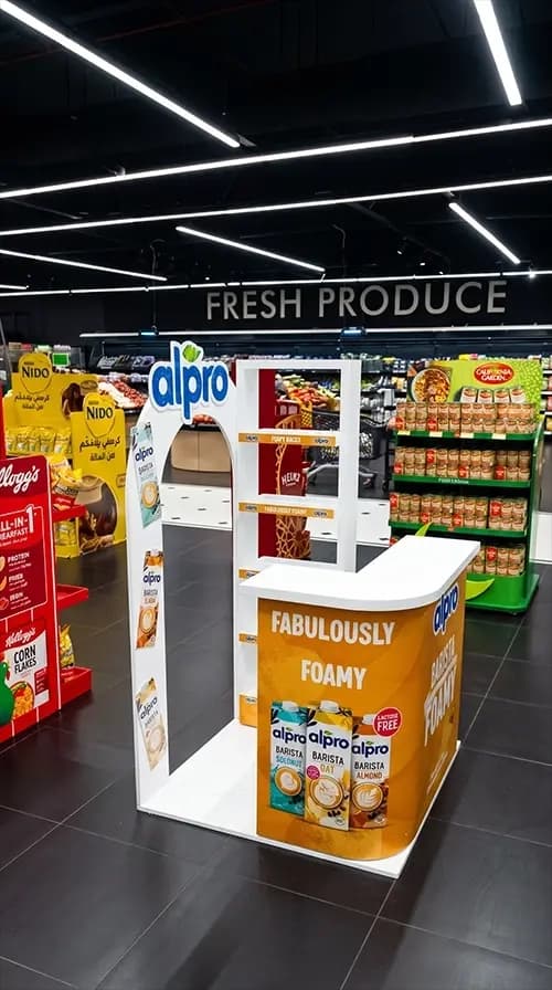 Alpro sampling stand positioned beside the fresh produce section of a supermarket