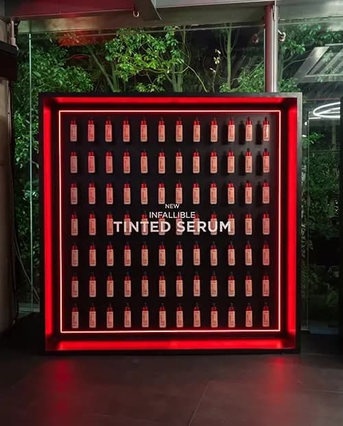 Illuminated grid wall holding L'Oréal tinted serum bottles in a red light frame