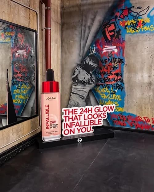 Oversized L'Oréal tinted serum replica on a plinth against a graffiti wall