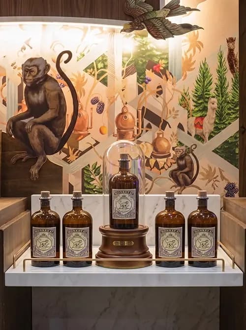 Monkey 47 bottles on a display podium under a glass dome against a printed botanical mural